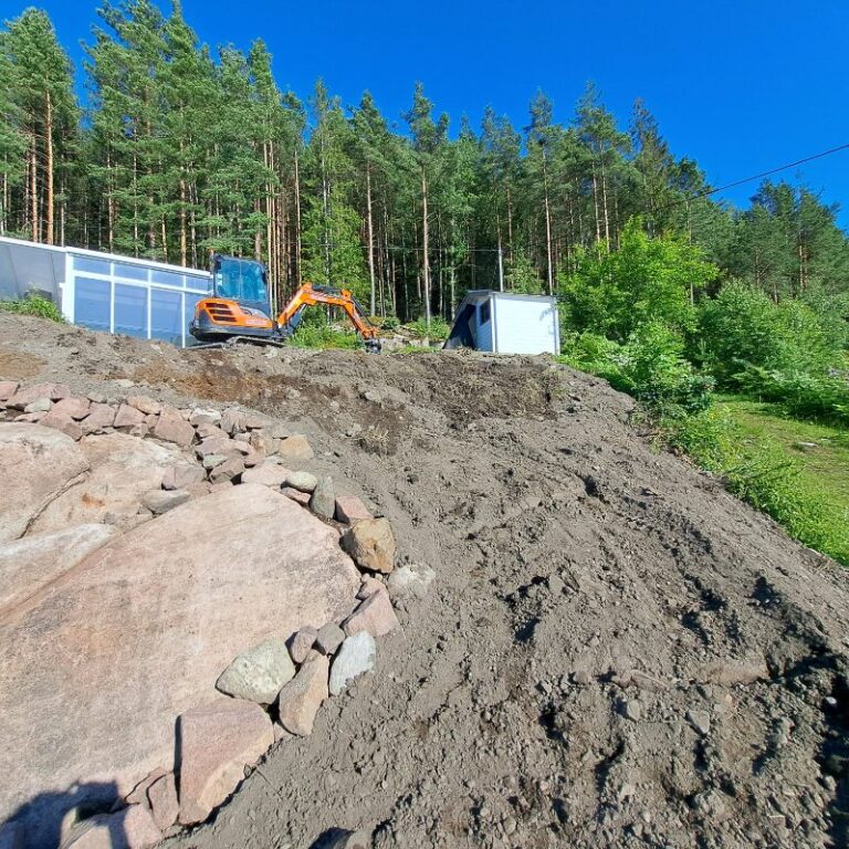 Gravemaskin, jordmasser og fjell på en tomt under grunnarbeid